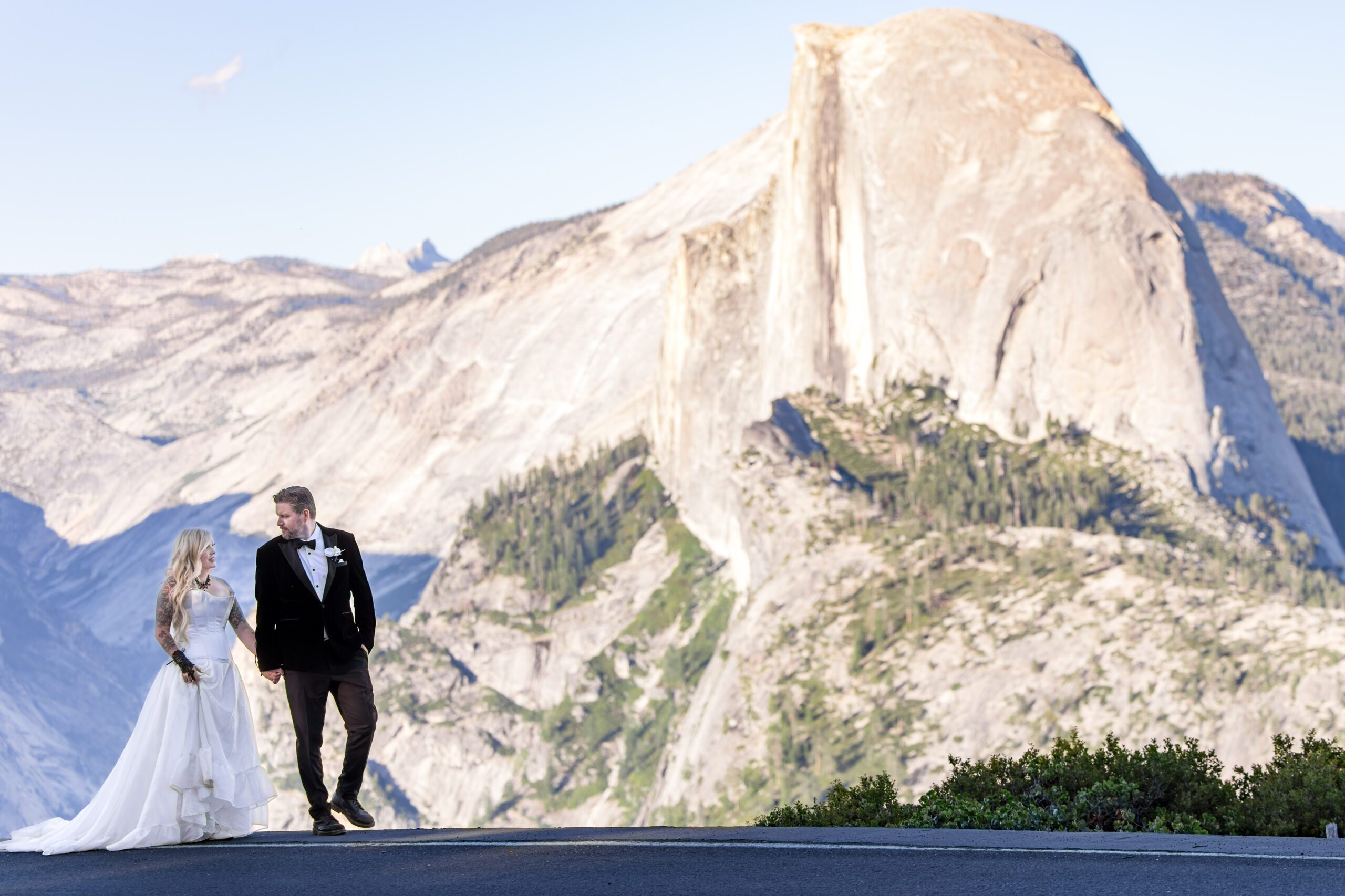 Couple walk along the side of the road at Glacier Point in Yosemite National Park with Half Dome off in the distance